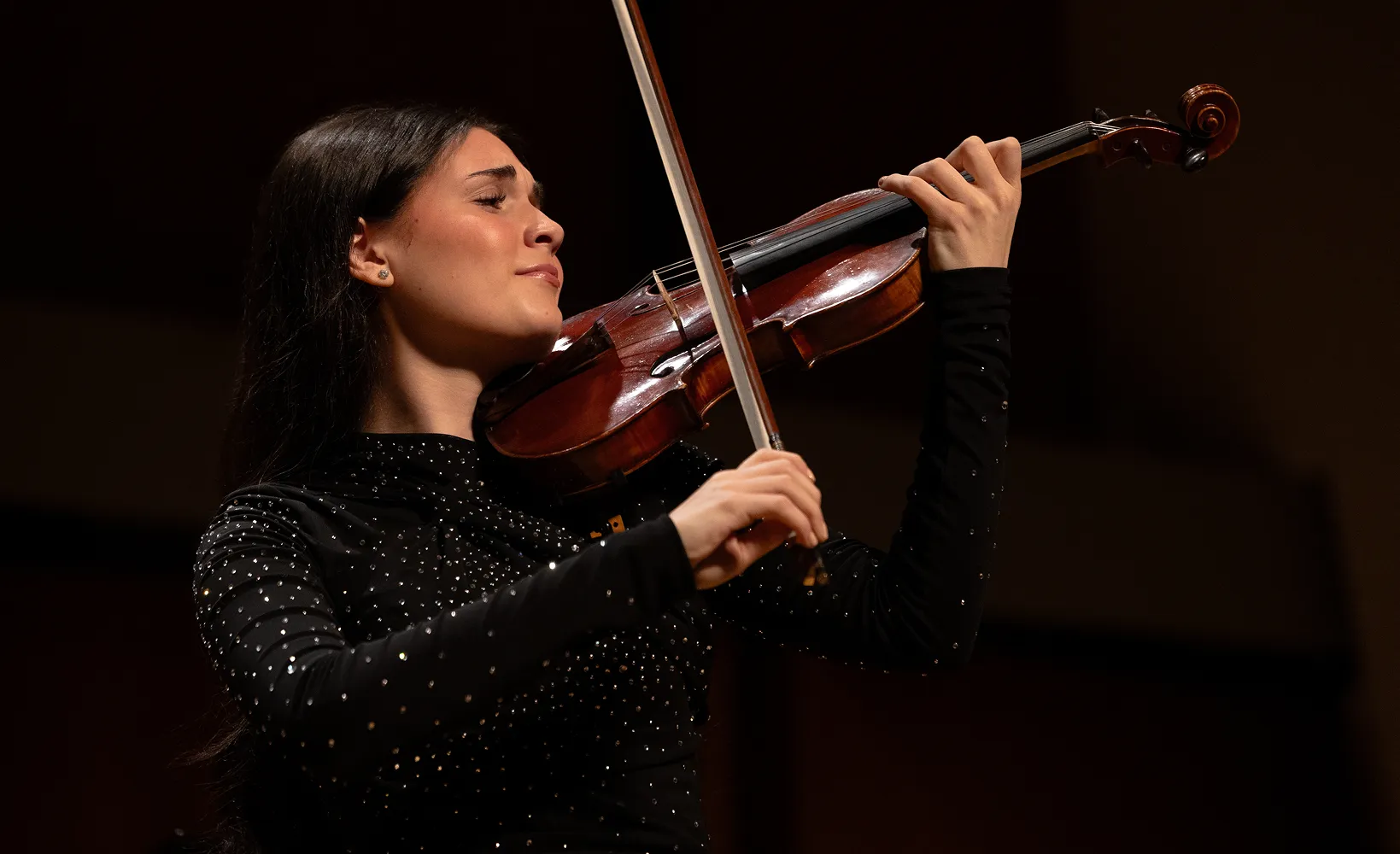 Nesya playing violin on stage under dramatic lighting