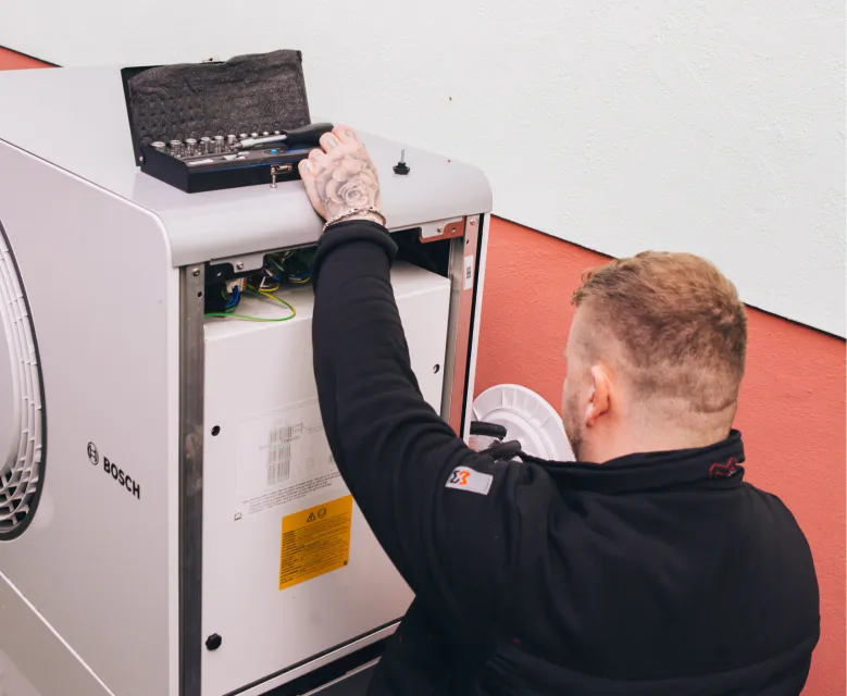 Techniker mit Tattoo an der Hand arbeitet an einer Bosch-Heizungsanlage mit geöffnetem Werkzeugkoffer obenauf.