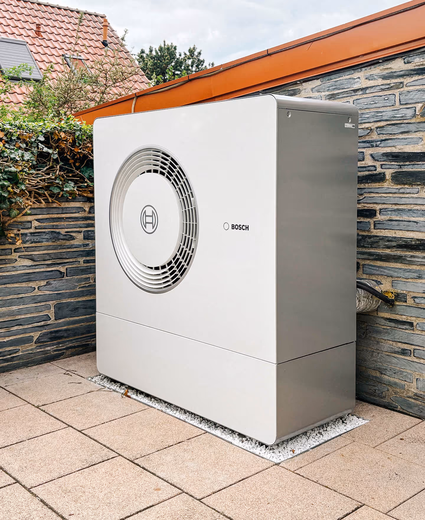 Lächelnder älterer Mann zeigt Daumen hoch neben einer Bosch-Außenwärmepumpe vor einem Haus.