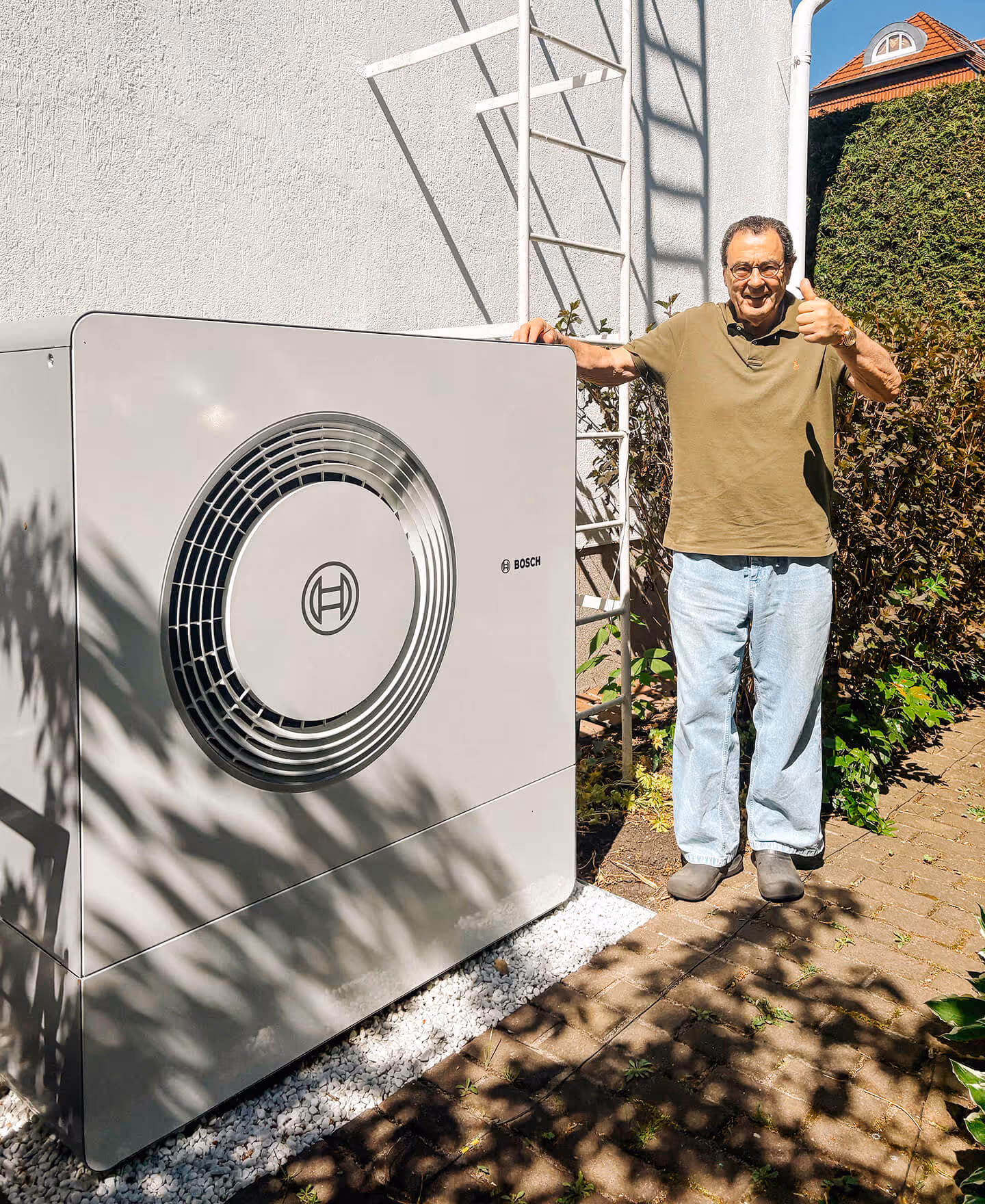 Mann steht draußen neben einer Bosch-Wärmepumpe und zeigt Daumen hoch.