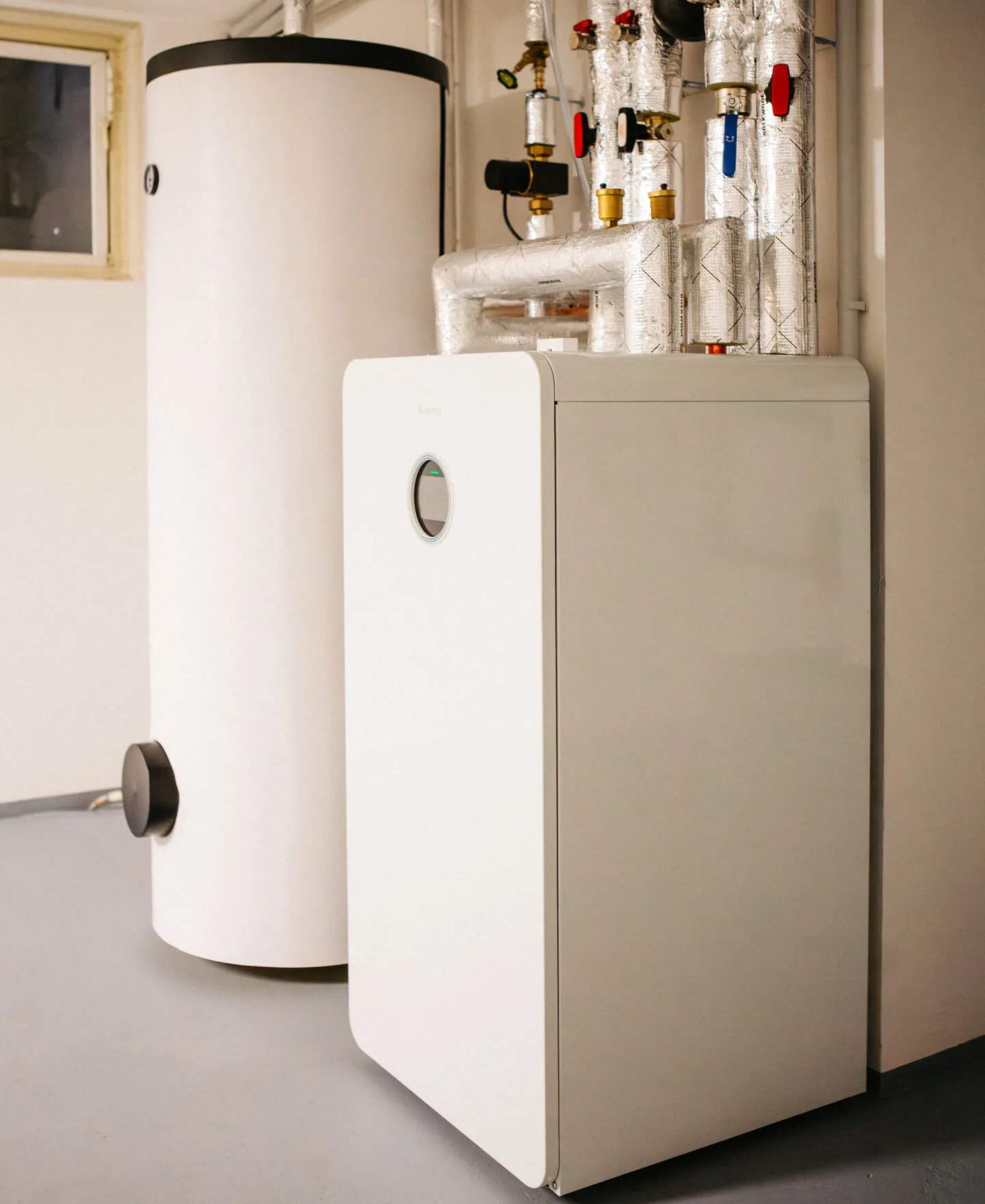 Moderne weiße Wärmepumpe mit isolierten Rohren in einem Heizungsraum installiert.