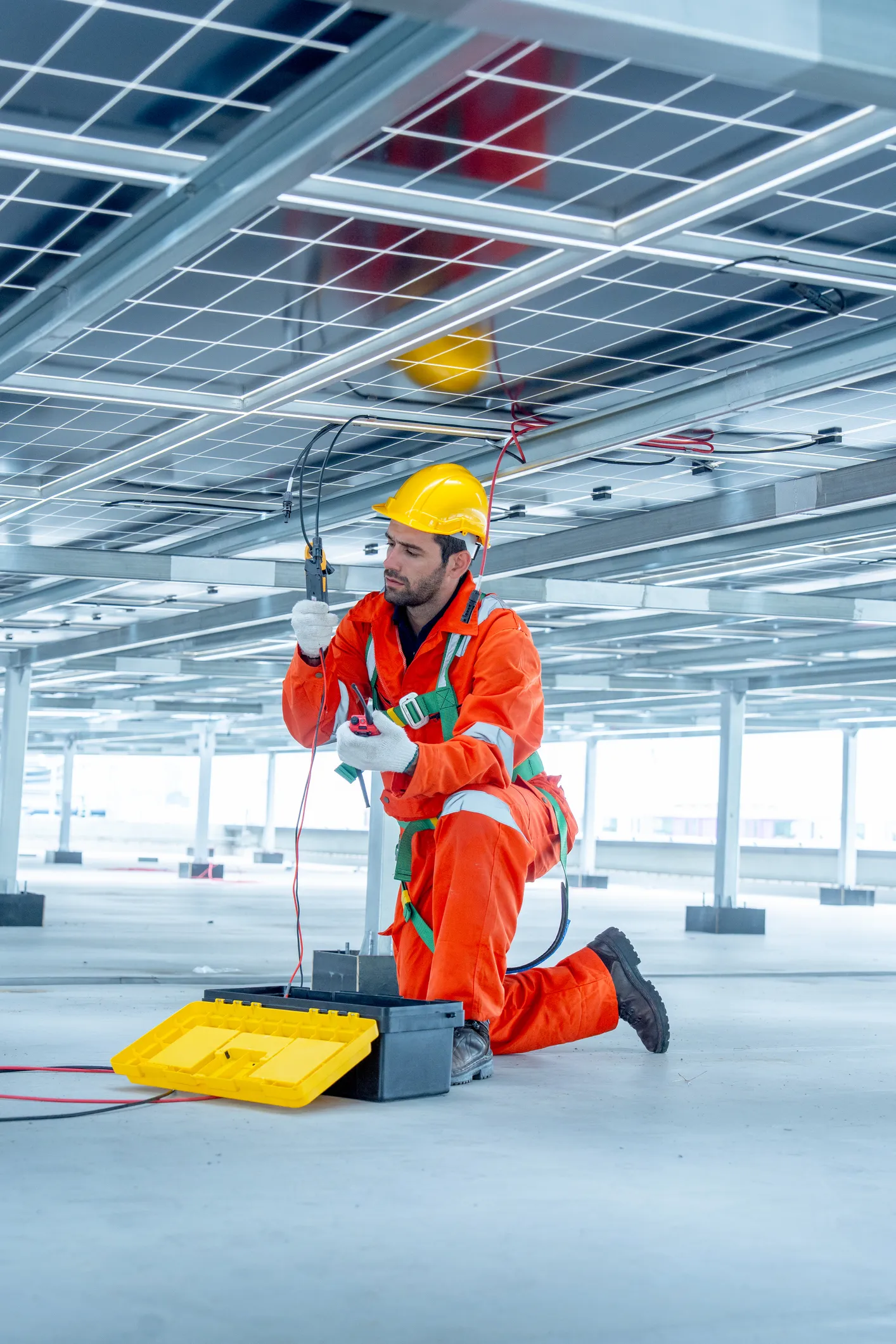 Electrician in coveralls testing equipment at a commercial solar installation