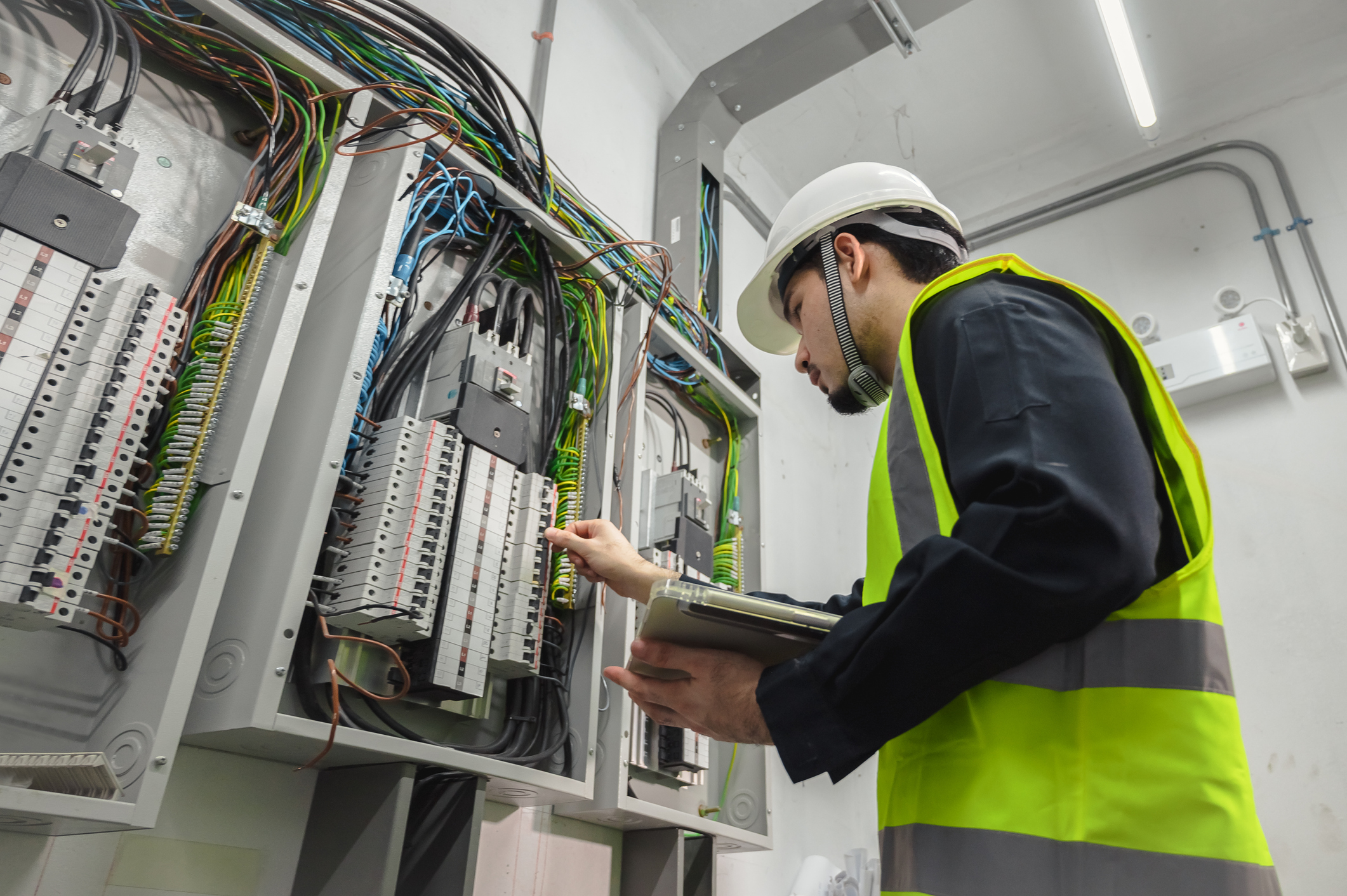 Electrician inspecting a distribution panel with a tablet