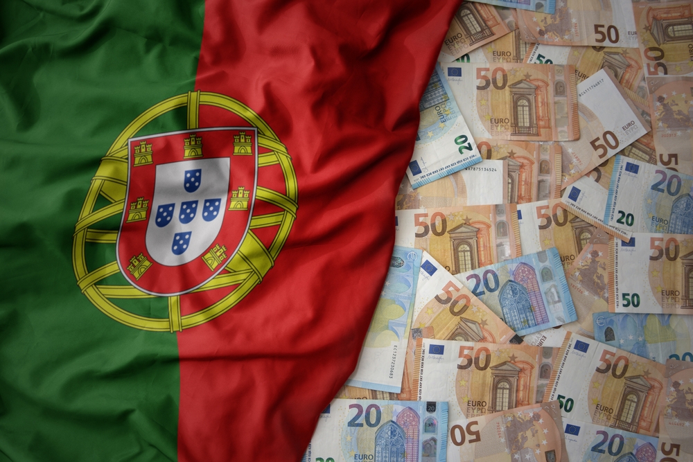 A collection of Euro banknotes spread across a surface, partially covered by a wrinkled flag of Portugal