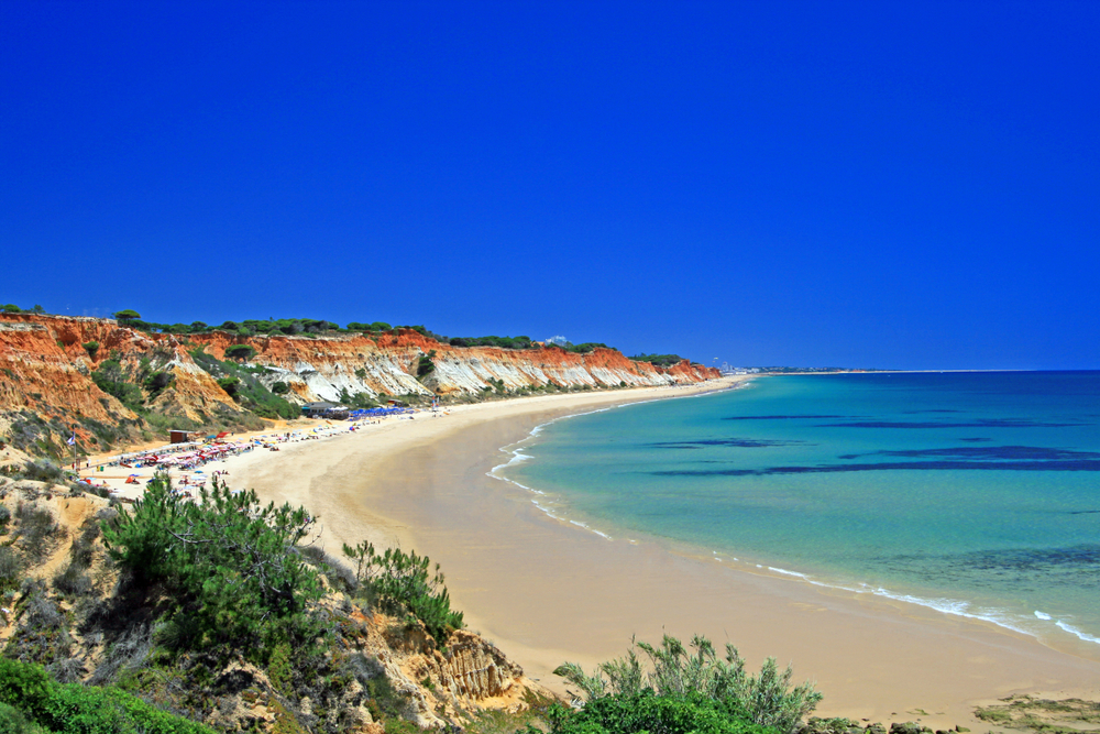 Vibrant orange and white cliffs border a long, sandy beach and bright turquoise water