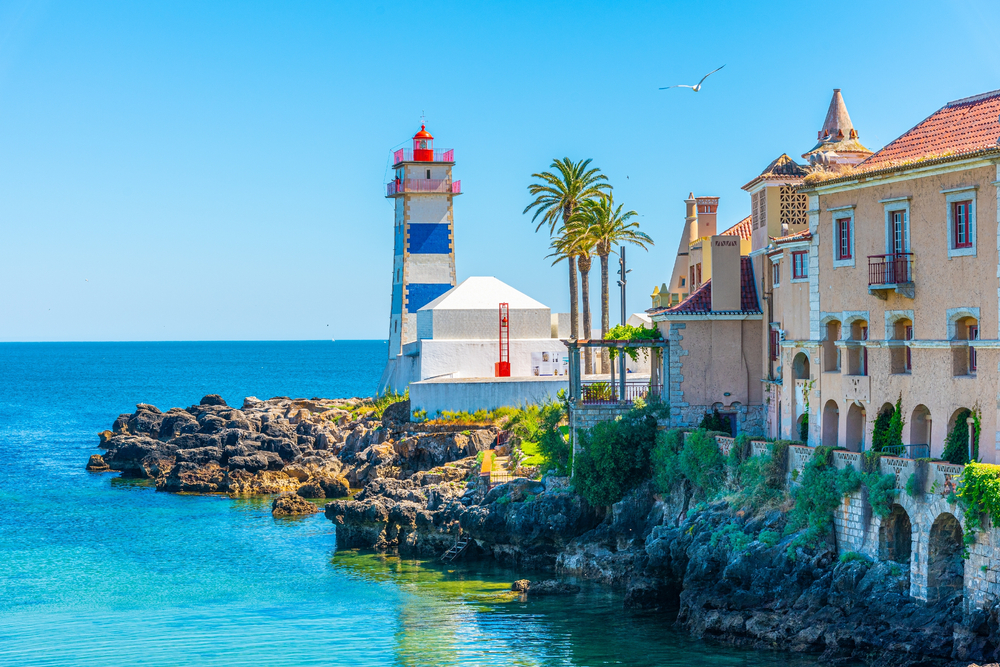 Blue and white Santa Marta Lighthouse on a rocky Cascais coastline under a clear summer sky