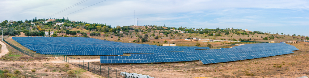 A wide panorama of a large solar panel field under a pale sky in a rural landscape