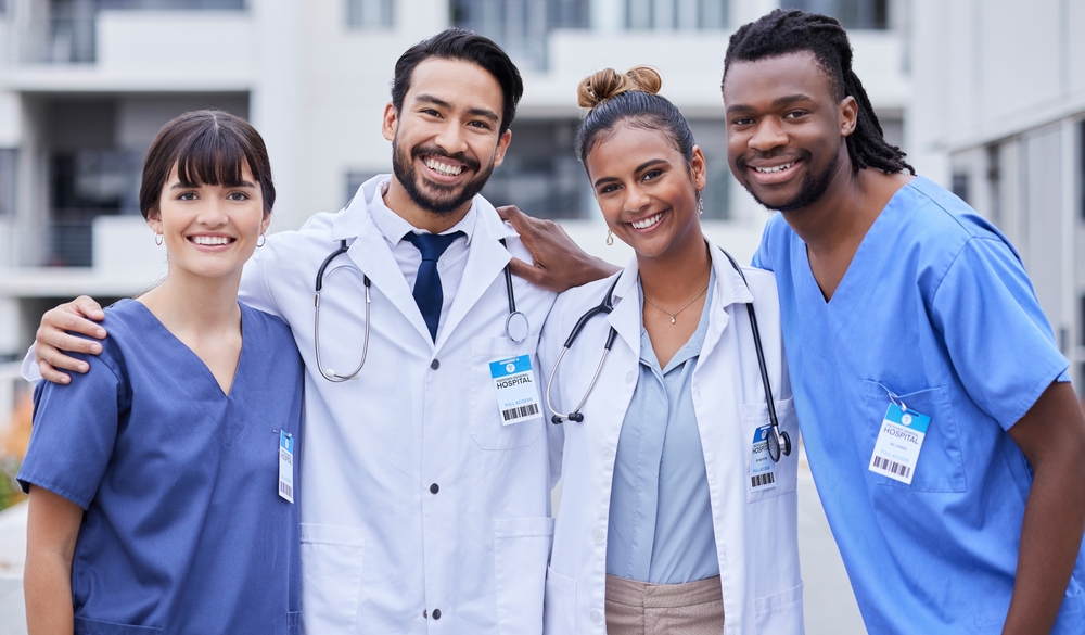 Four happy doctors and nurses smiling in front of a hospital building