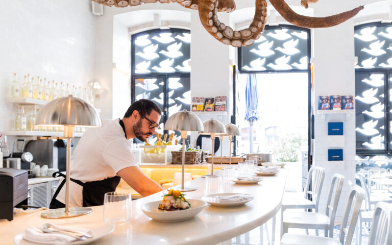 Modern bright restaurant counter with a chef preparing a dish under a large octopus decor