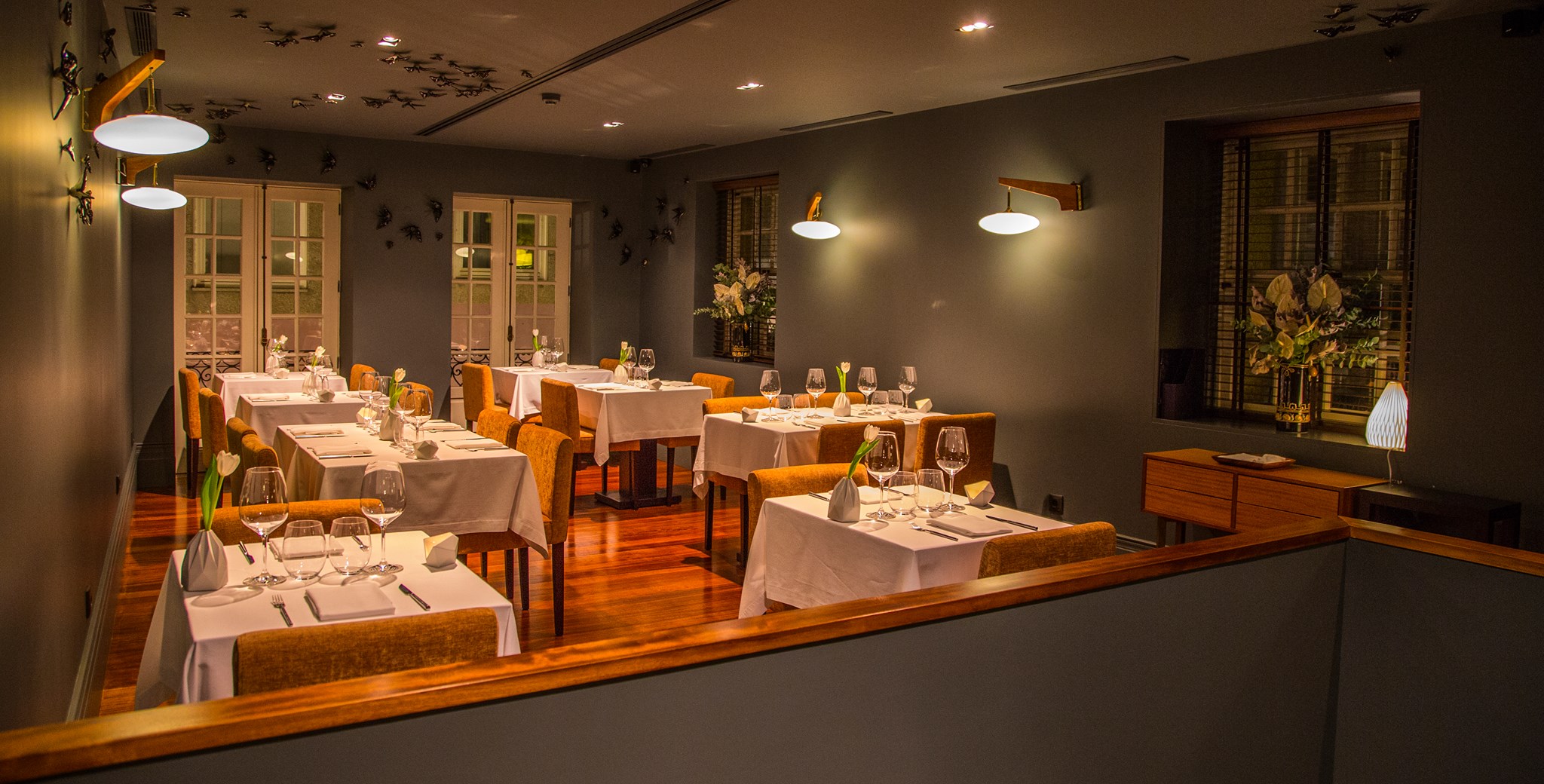Modern fine dining room with grey walls warm lighting and white tablecloths on small tables