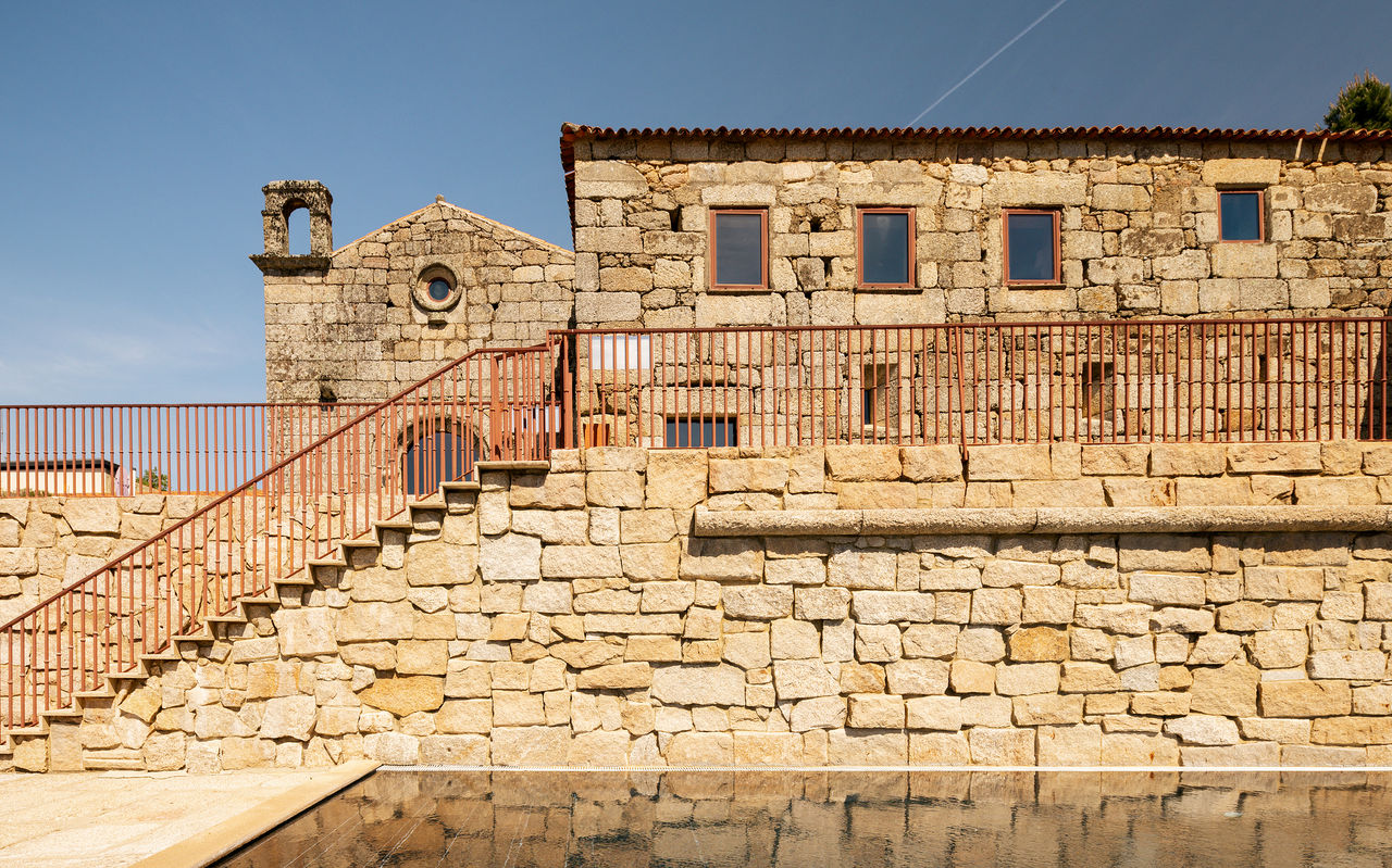 Historic stone building with a small church and a swimming pool in the foreground