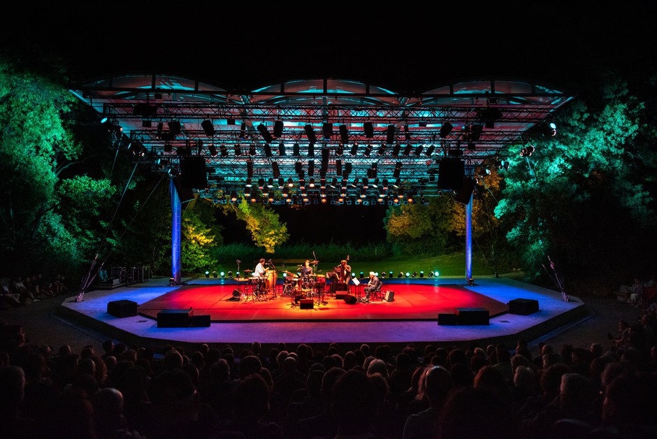azz band performing on a red-lit outdoor stage at night in front of a large audience