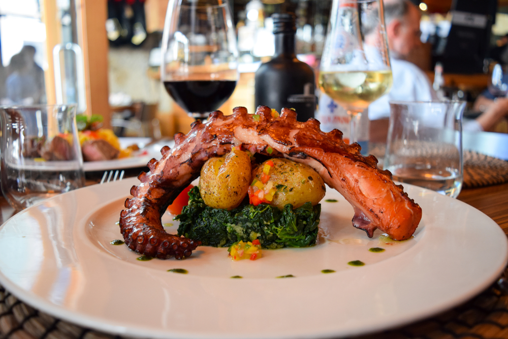 Gourmet grilled octopus tentacle served over greens and potatoes in a bright restaurant