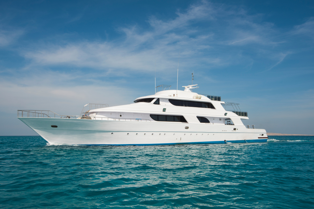Luxurious white motor yacht cruising on calm turquoise ocean water under a clear blue sky