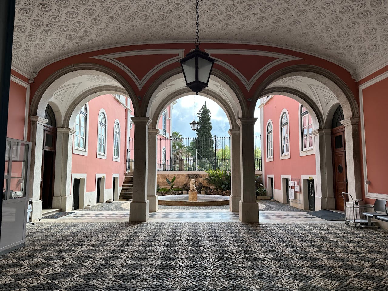 An elegant palace courtyard with pink walls, marble arches, and a central stone fountain
