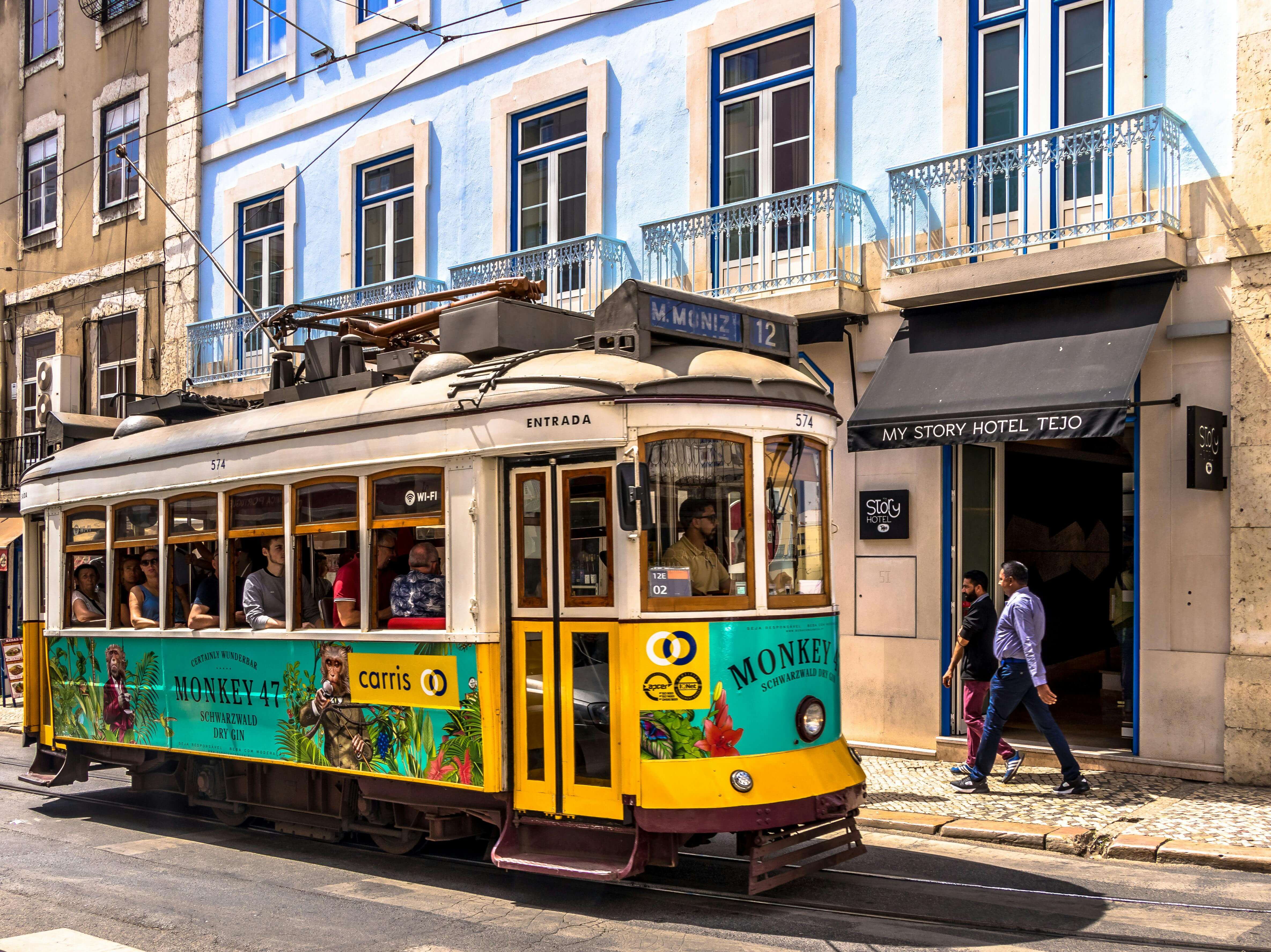 Yellow and white tram passing 'My Story Hotel Tejo' on a sunny street in Lisbon