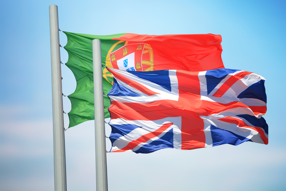 Flags of Portugal and the United Kingdom flying from white poles against a blue sky