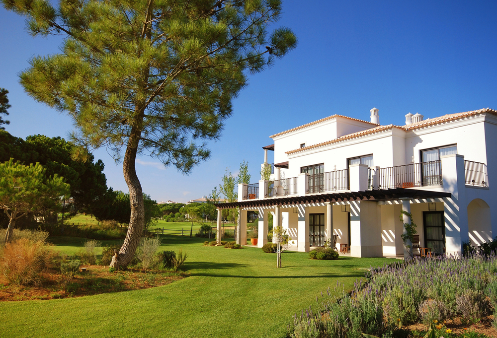 Luxury white villa in Portugal featuring a large pine tree and lush green garden