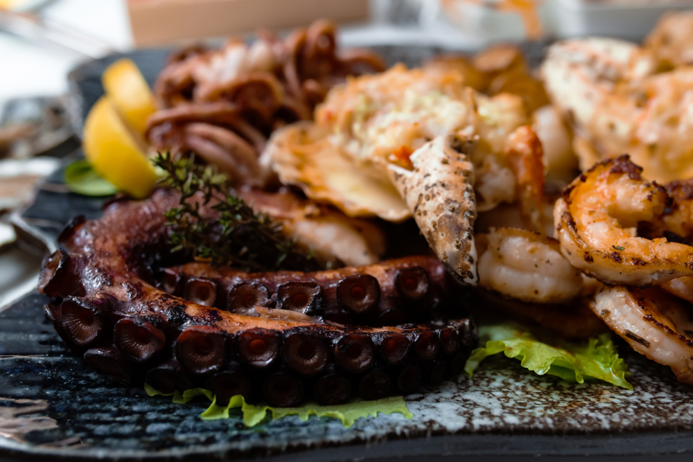 Gourmet seafood platter with grilled octopus tentacles shrimp and crab claw on a dark plate