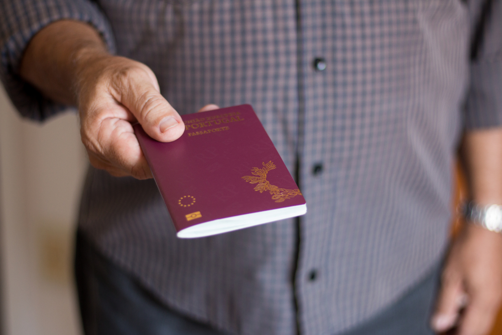 A person's hand extending a Portuguese biometric passport featuring gold foil national emblems