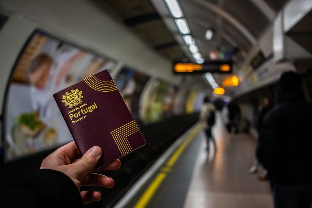 A hand holding a Portuguese passport on a subway platform at an underground station