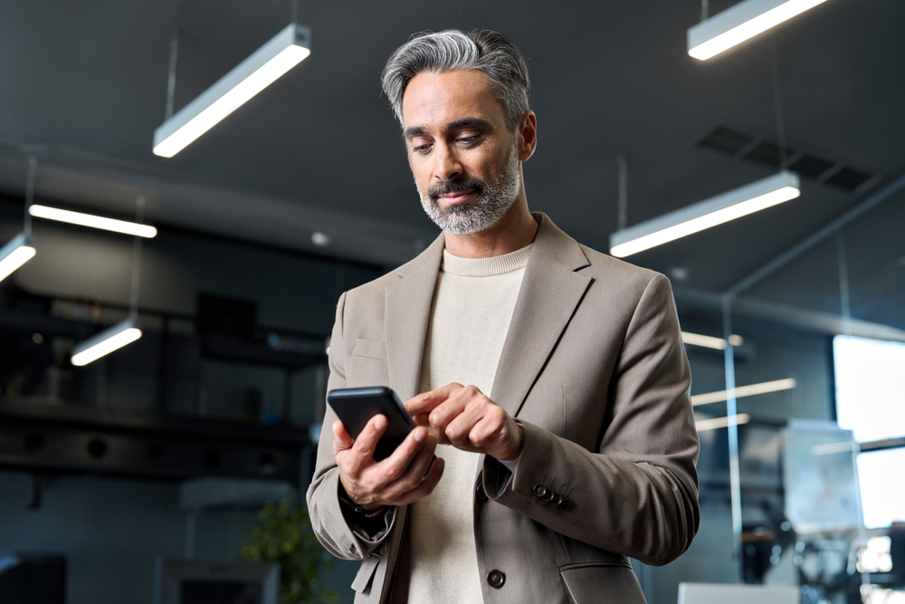 Mature professional man with grey hair using a smartphone in a modern office setting