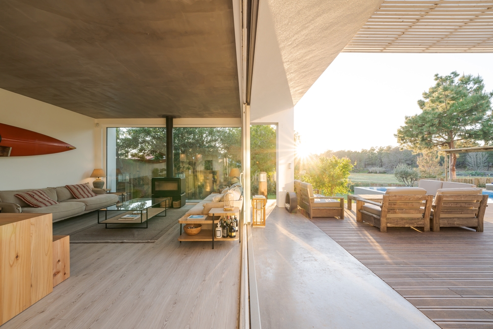 Modern living room opening onto a wooden sun deck with a pool and lush garden