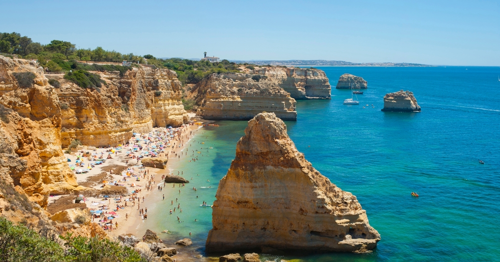 Crowded sandy Marina Beach in Lagoa with tall golden limestone cliffs and turquoise water
