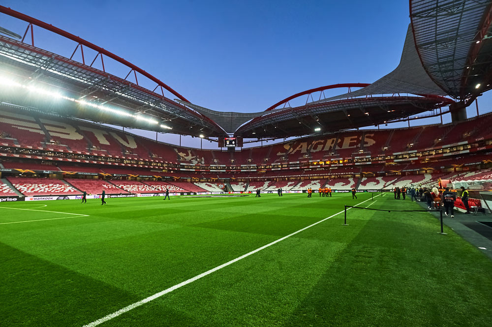 Wide view of Lisbon's Estadio Da Luza football stadium with red seats and lush green pitch