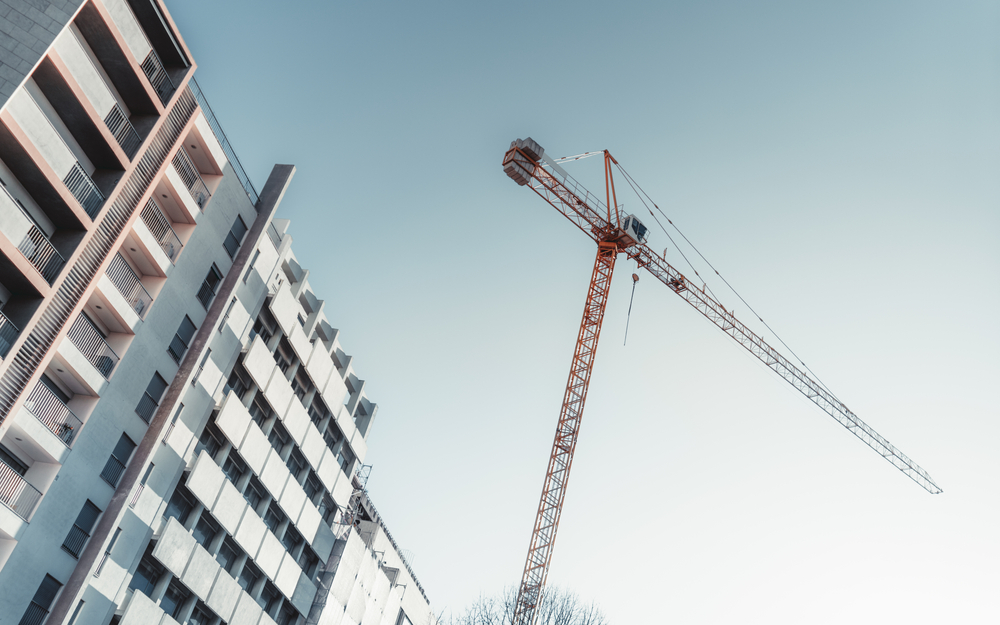 Low-angle view of an orange construction crane beside a modern, multi-story apartment block