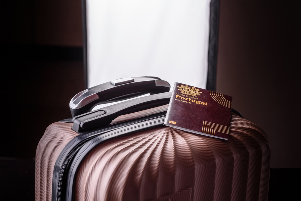 A Portuguese passport resting on the handle of a bronze-coloured hardshell suitcase