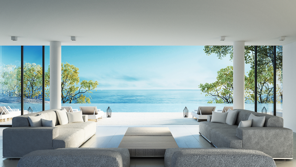 Modern living room with grey sofas facing a wide ocean view and an infinity pool outside