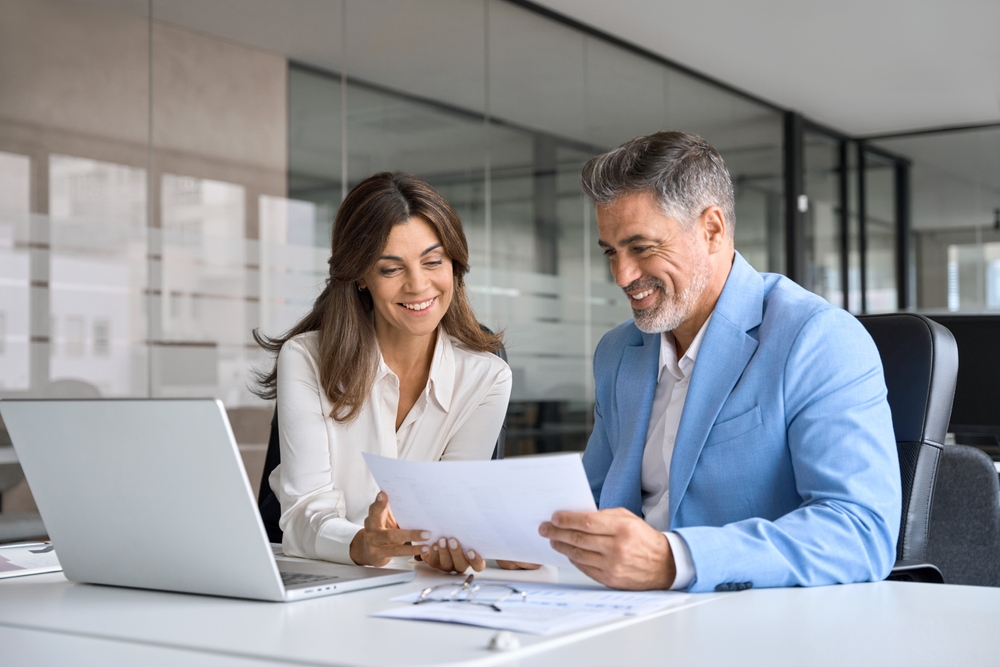 Two smiling professionals in an office reviewing a document together at a desk