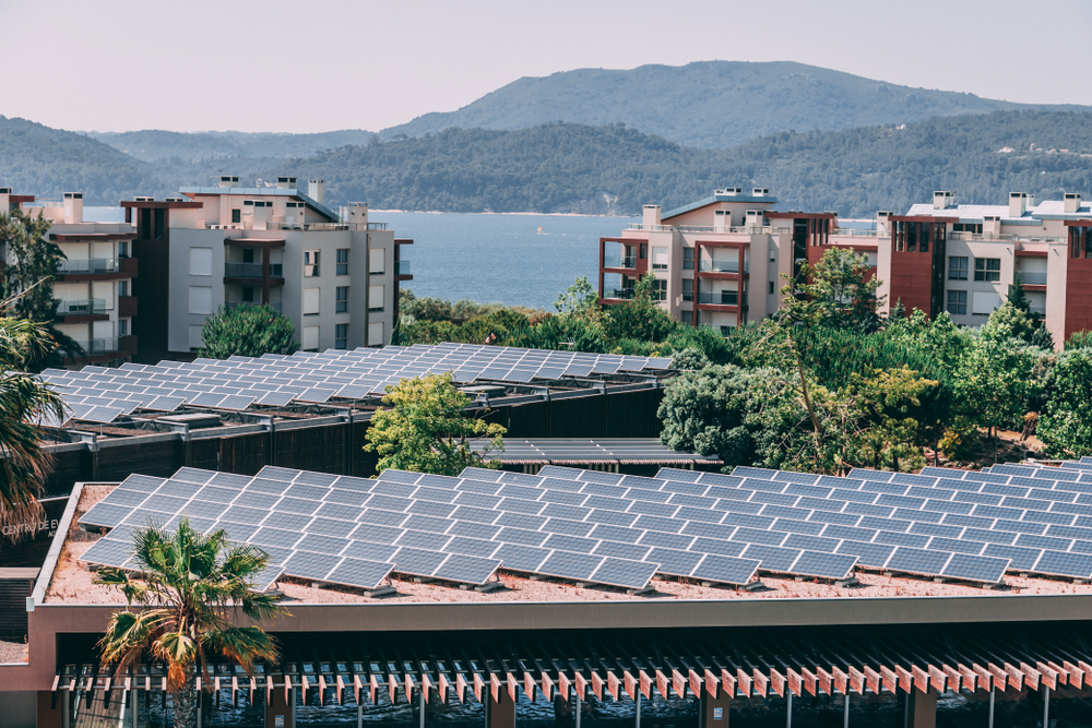 Rooftop solar panels on modern buildings by the sea with tree covered hills in the distance