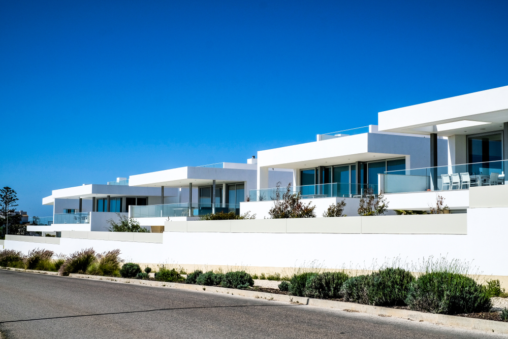 A row of sleek white coastal villas with glass balconies along a road in the bright Portuguese sun