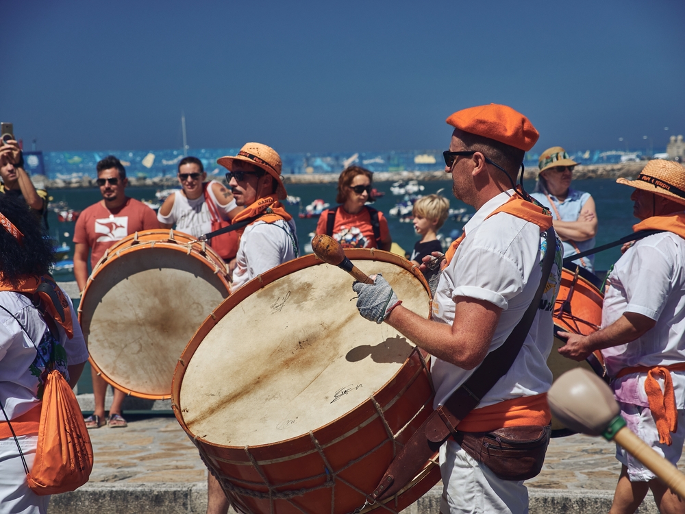 Musicians in orange berets playing traditional bass drums in a seaside street parade celebration