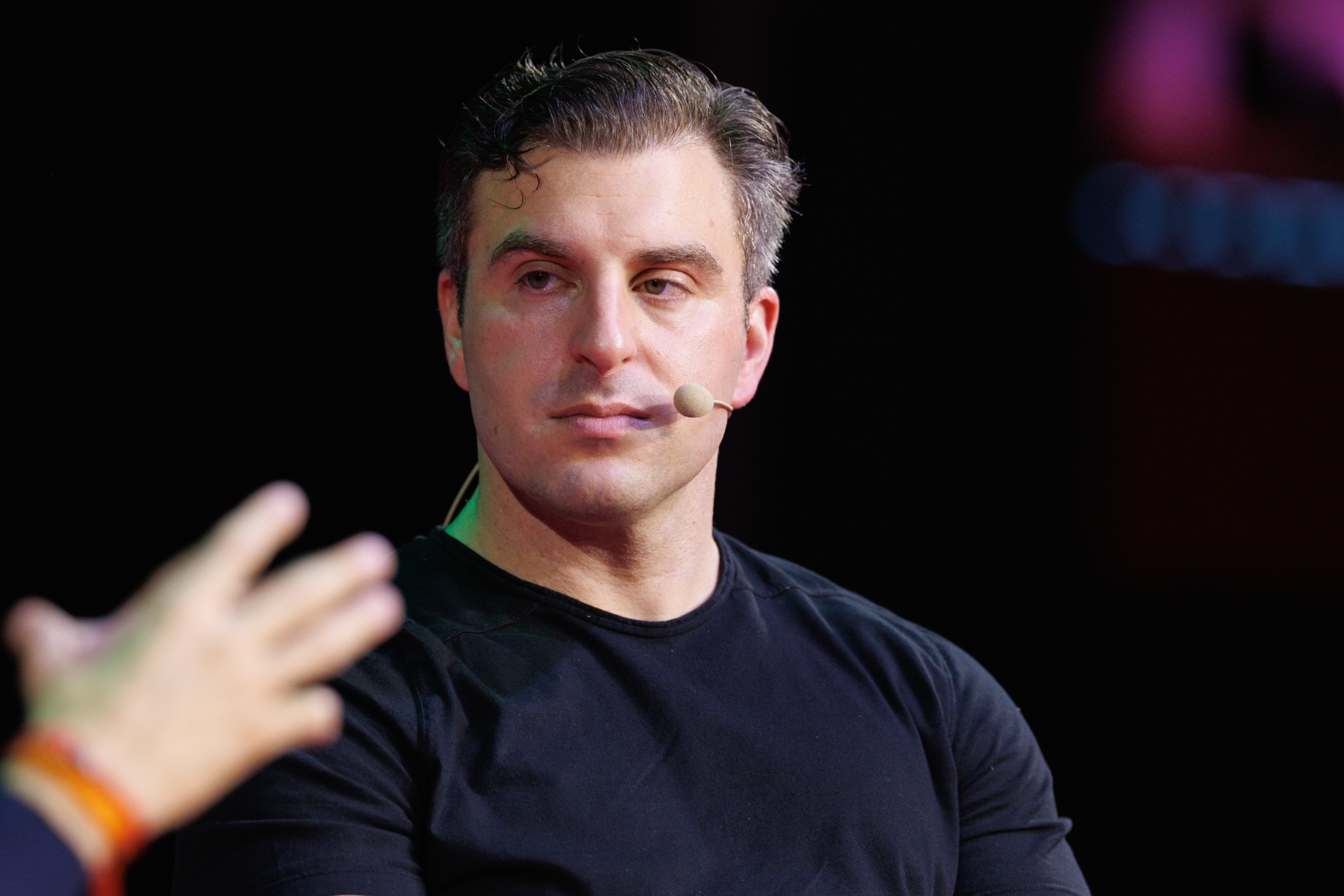 Airbnb CEO Brian Chesky speaking on stage with headset mic