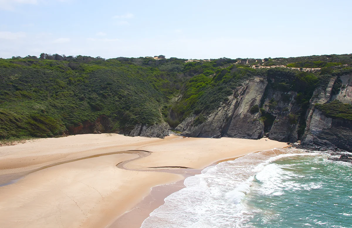 Secluded sandy cove nestled against dramatic dark cliffs on the Portuguese coast