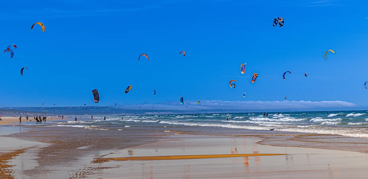 Kitesurfers riding Atlantic waves under colorful kites at Fonte da Telha beach