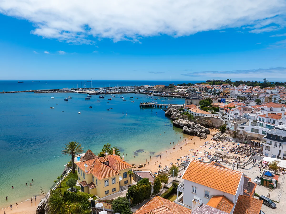 Sunny view of Praia da Rainha beach, historic villa, and the marina in Cascais