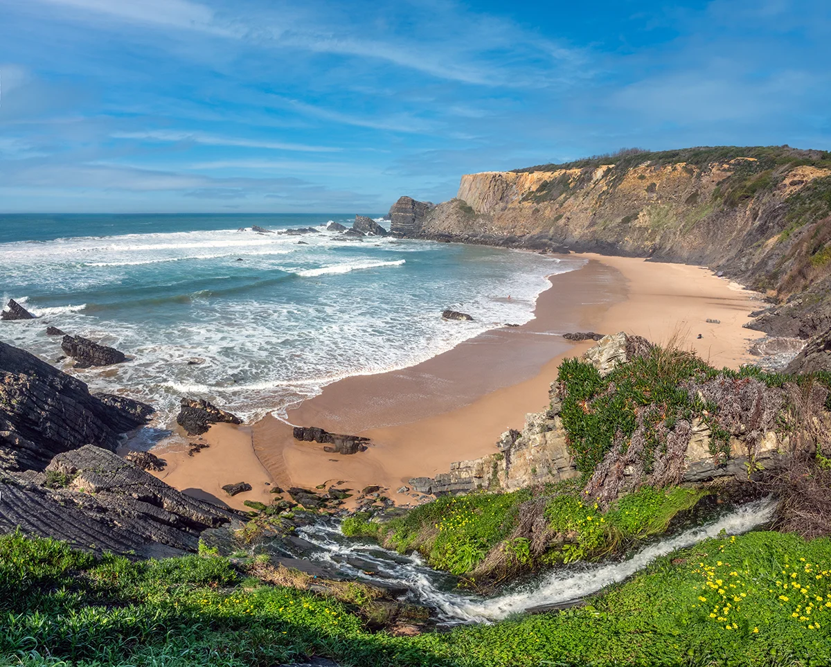 Scenic waterfall flowing onto Praia da Amalia beach and rocky ocean cliffs in Portugal