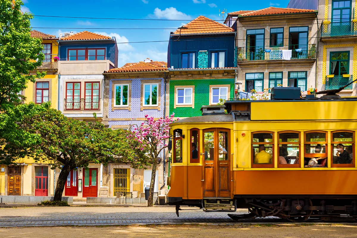 Yellow vintage tram passing colorful traditional tiled buildings in Porto city centrer