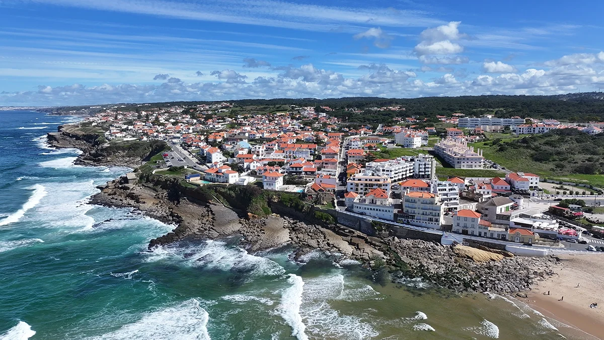 Ocean waves crash against the rocky shore of a coastal town with red-roofed houses
