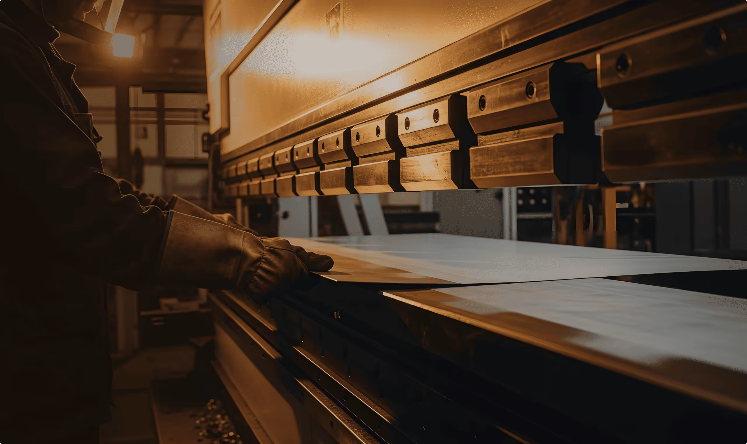 Worker wearing gloves operating a metal bending machine in a fabrication workshop.