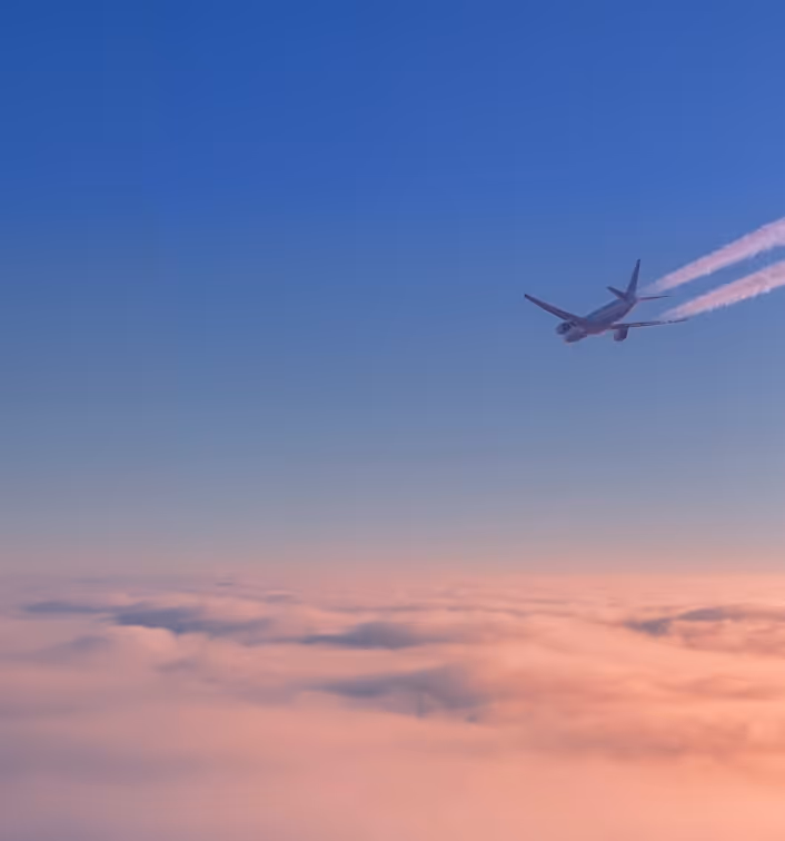 Airplane flying above pink clouds with blue sky and contrails at sunset.