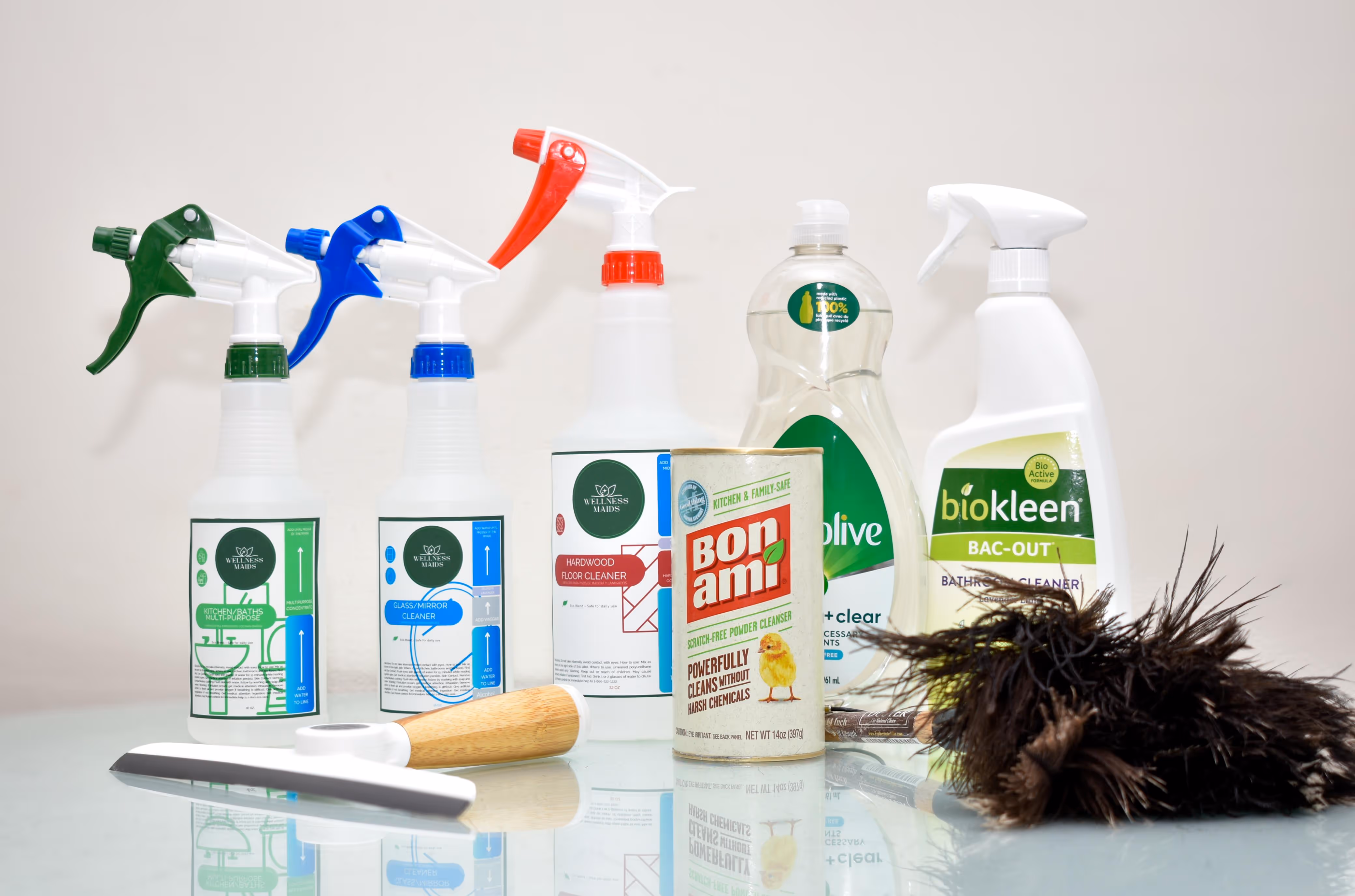 Various cleaning products including spray bottles, a powder cleanser, dish soap, and cleaning tools on a reflective surface.