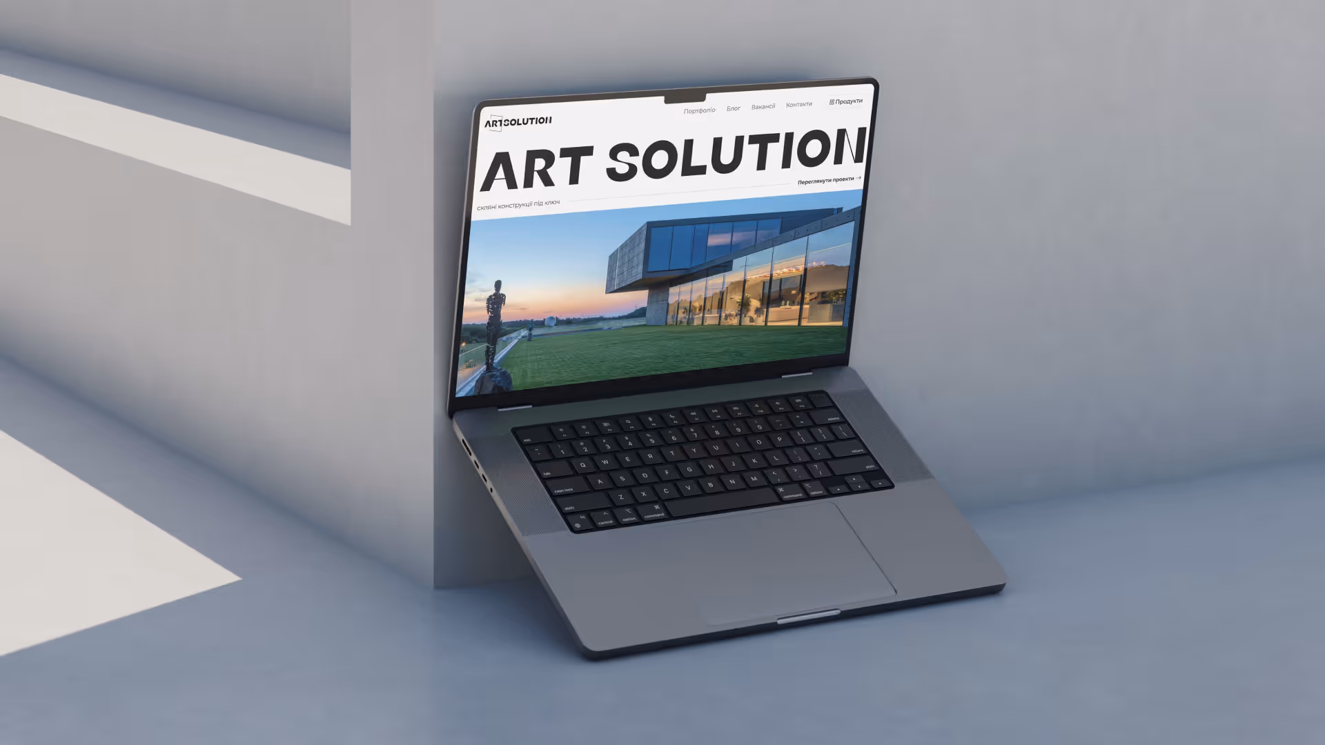 Ноутбук із відкритим сайтом Art Solution, на екрані зображено сучасну будівлю з великим скляним фасадом і зелену галявину.