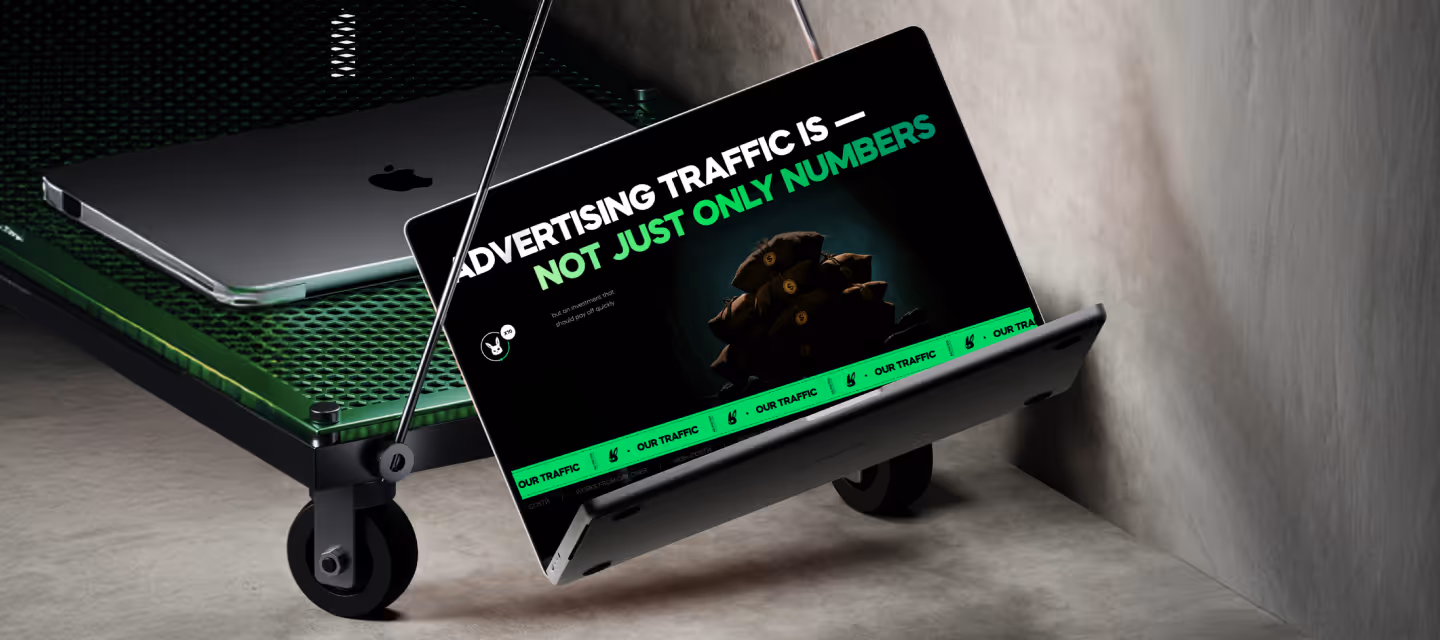 Ноутбук, підвішений на металевому візку, з екраном, що показує текст "Advertising traffic is — not just only numbers" та зображення грошових мішків.