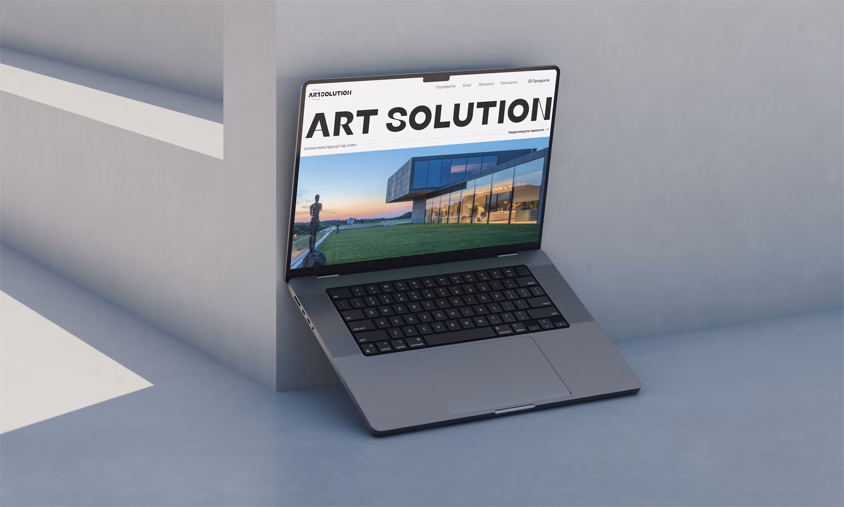 Відкритий ноутбук із вебсайтом ART SOLUTION, що показує сучасну будівлю зі скляними фасадами на екрані.