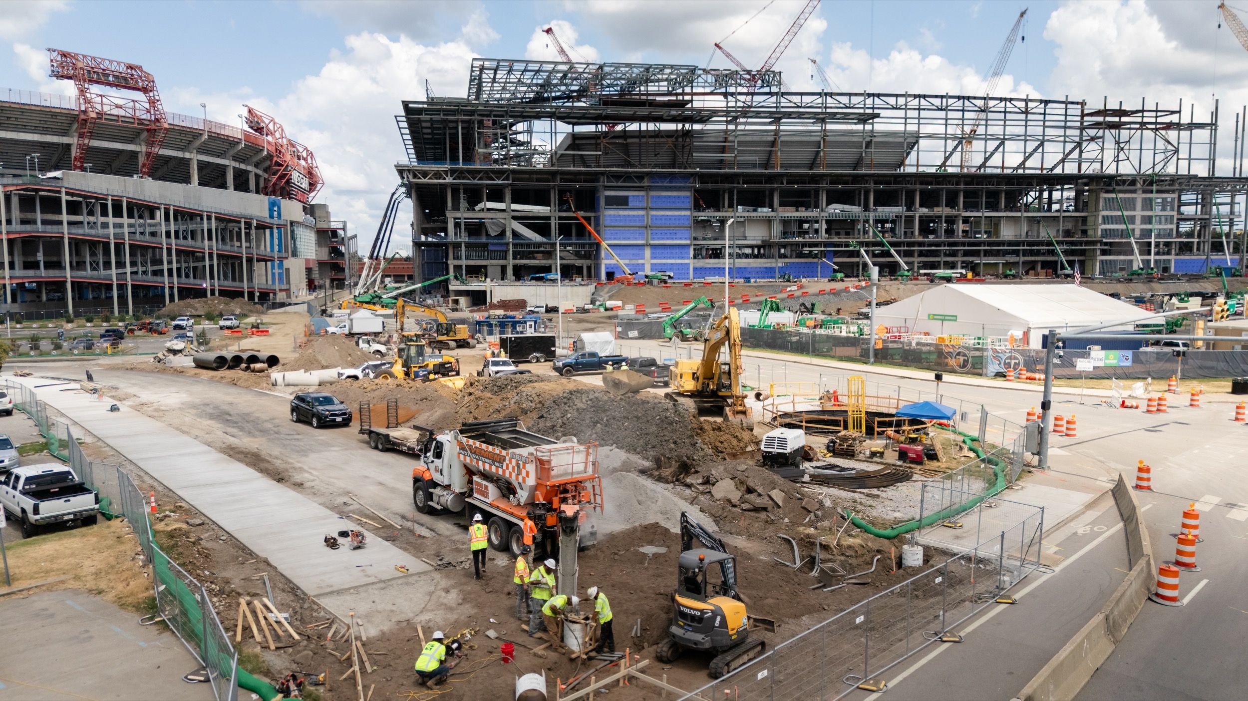 Construction site with workers, heavy machinery, and large buildings under construction on a partly cloudy day.